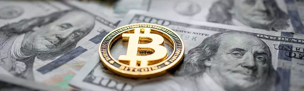 a symbolic bitcoin sitting on some $100 bills