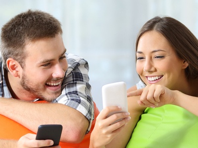 two friends playing on their phones together resting on floor pillows